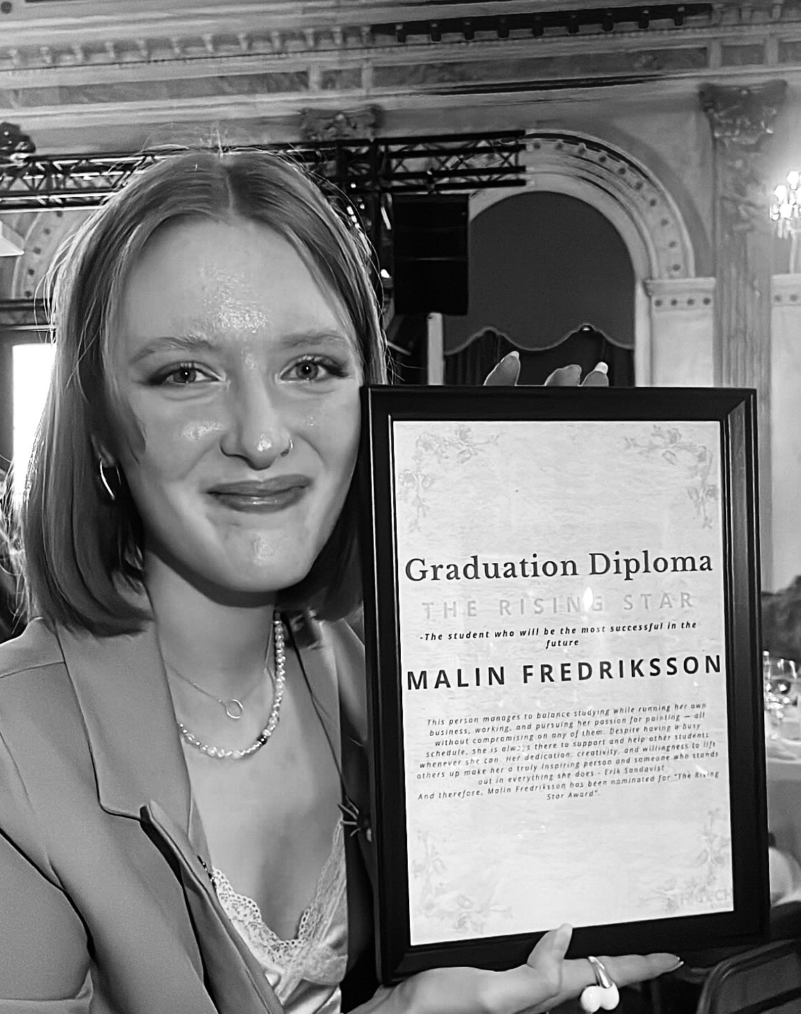 Photography of Malin Fredriksson, sitting on a chair smiling at the camera with her diploma rising star.